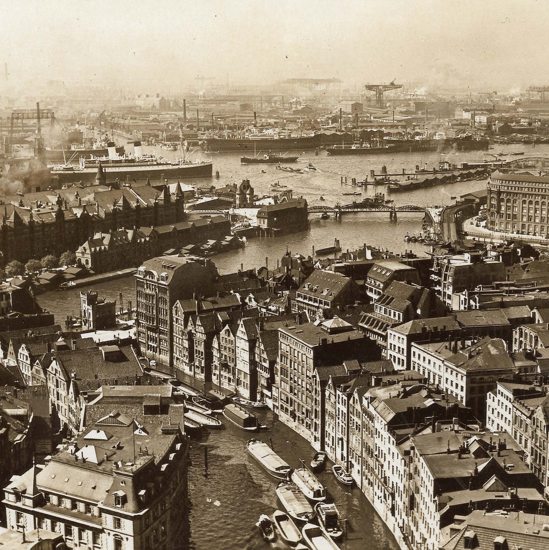 Historische Stadtansicht mit Hafen, Schiffen und alten Gebäuden in sepiafarbenem Ton.
